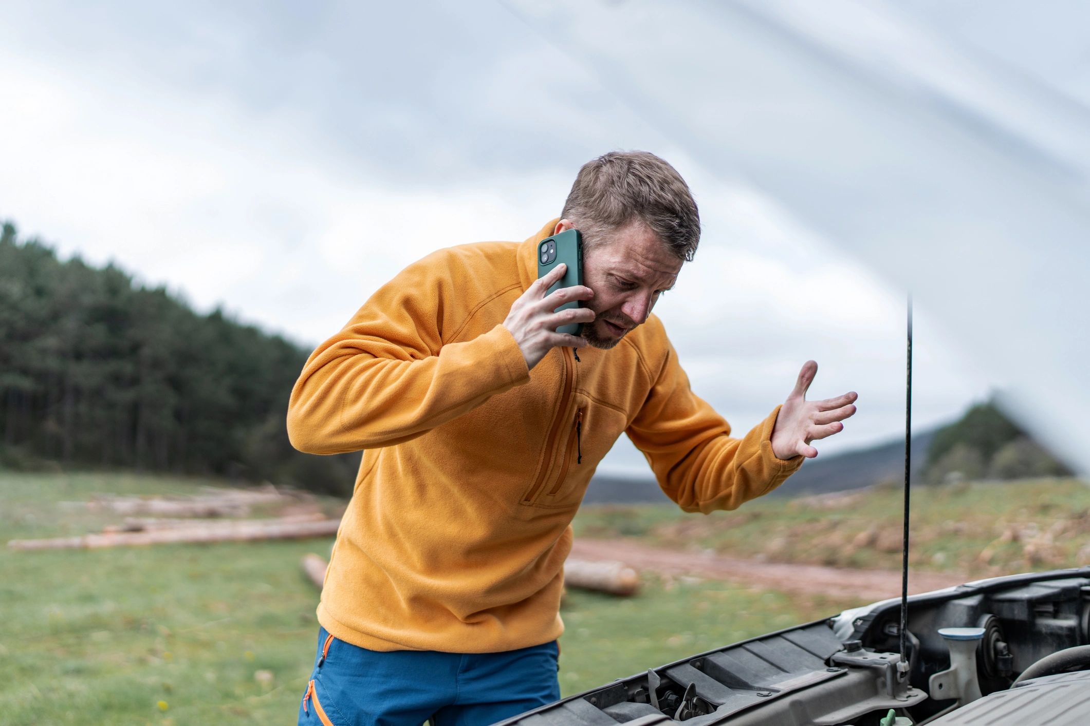 Driver calling for roadside assistance beside broken down car